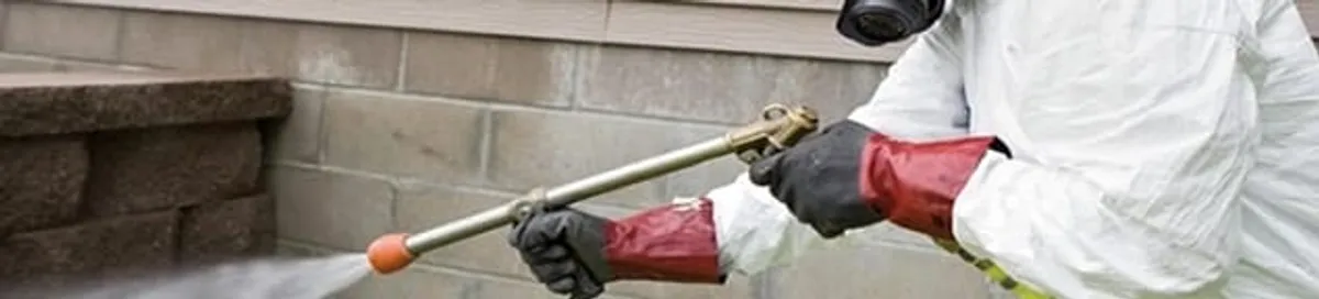 Pest control technician applying exterior insect treatment along a home foundation in Atlanta, GA