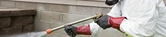 Pest control technician applying exterior insect treatment along a home foundation in Atlanta, GA