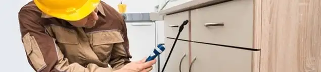 Roach exterminator applying treatment under kitchen cabinets in Atlanta, GA