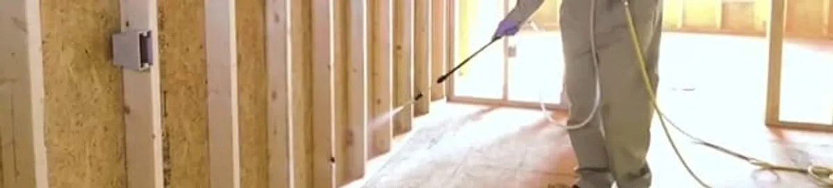Termite treatment technician applying spray along framing and unfinished walls in Atlanta, GA