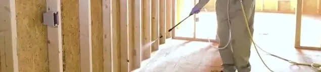 Termite treatment technician applying spray along framing and unfinished walls in Atlanta, GA