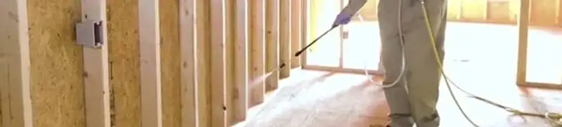 Termite treatment technician applying spray along framing and unfinished walls in Atlanta, GA